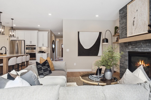 living room featuring wood-type flooring, a chandelier, and a stone fireplace