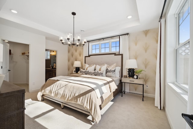 carpeted bedroom featuring a closet, a notable chandelier, ensuite bath, a raised ceiling, and a spacious closet