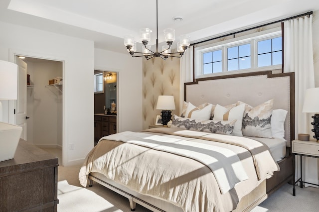 bedroom featuring light carpet, a closet, connected bathroom, a chandelier, and a walk in closet