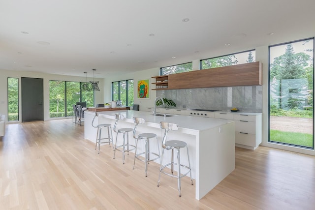 kitchen featuring decorative backsplash, sink, white cabinetry, and an island with sink