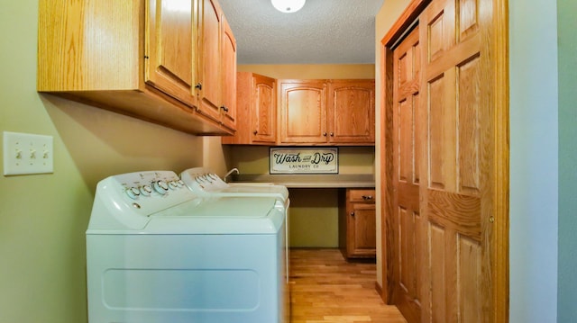 washroom with light wood-type flooring, a textured ceiling, washing machine and clothes dryer, and cabinets