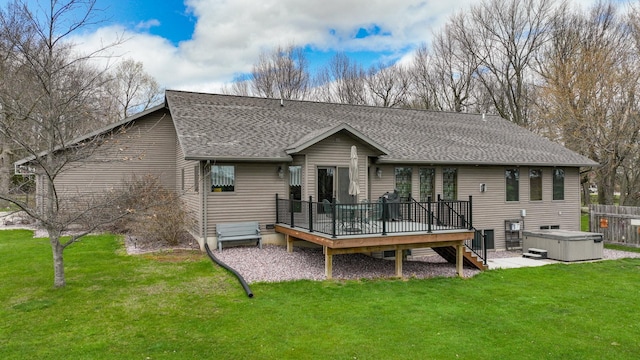 rear view of property featuring a lawn, fence, a shingled roof, a wooden deck, and a hot tub