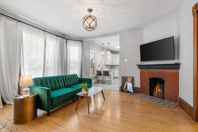 living room featuring a brick fireplace, sink, light hardwood / wood-style flooring, and a notable chandelier