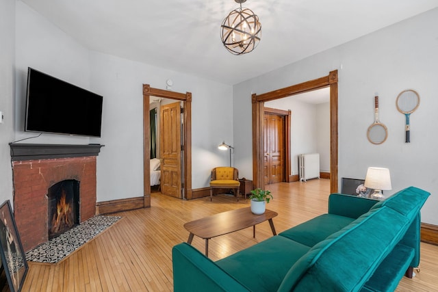 living room featuring a brick fireplace, light hardwood / wood-style floors, radiator, and a notable chandelier