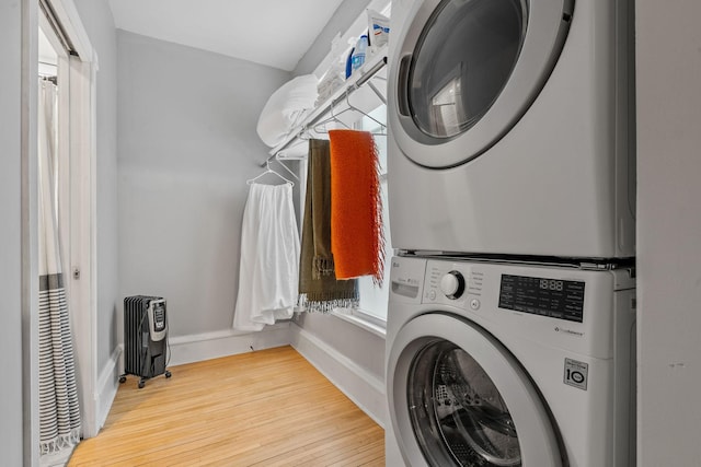 clothes washing area with stacked washing maching and dryer, radiator, and hardwood / wood-style flooring