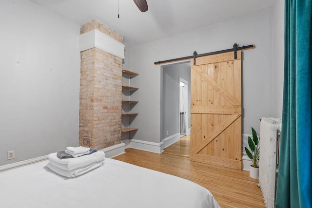 bedroom featuring ceiling fan, a barn door, and wood-type flooring