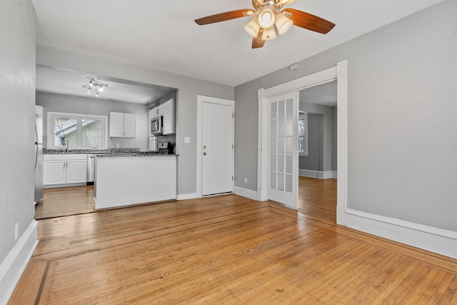 unfurnished living room featuring light wood-type flooring, ceiling fan, a textured ceiling, and sink