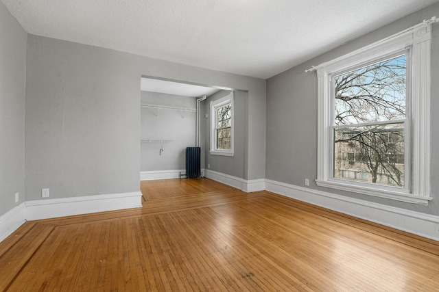 unfurnished living room featuring wood-type flooring, a wealth of natural light, radiator heating unit, and a textured ceiling