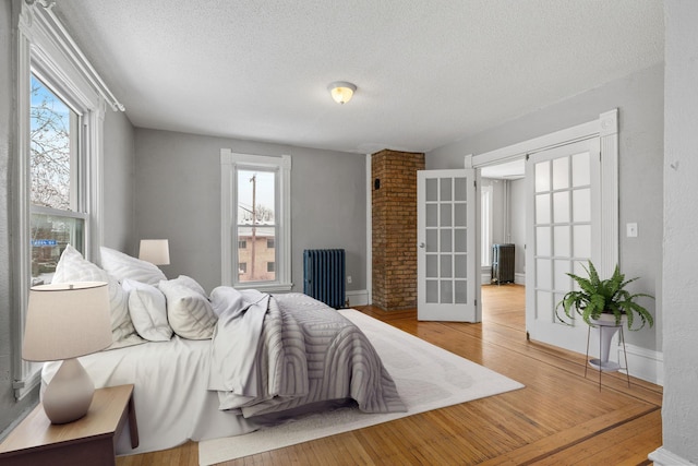 bedroom with french doors, radiator heating unit, a textured ceiling, and hardwood / wood-style flooring