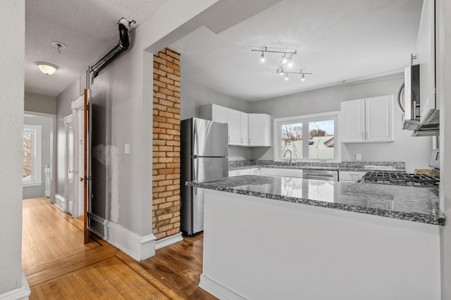 kitchen featuring kitchen peninsula, stainless steel appliances, a textured ceiling, white cabinets, and dark stone counters