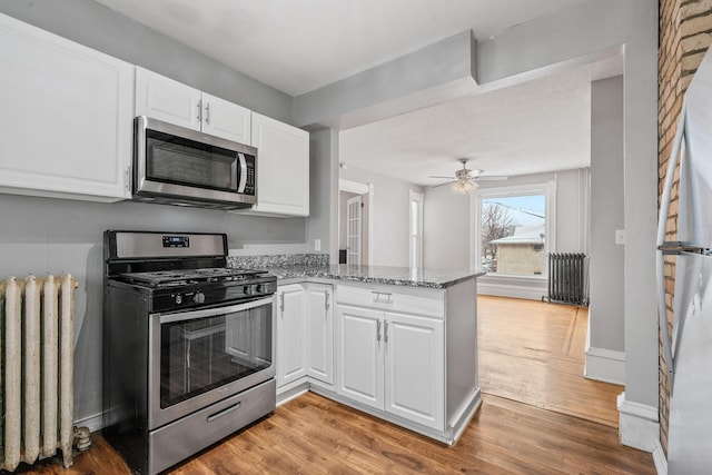 kitchen featuring radiator, kitchen peninsula, stainless steel appliances, and white cabinetry