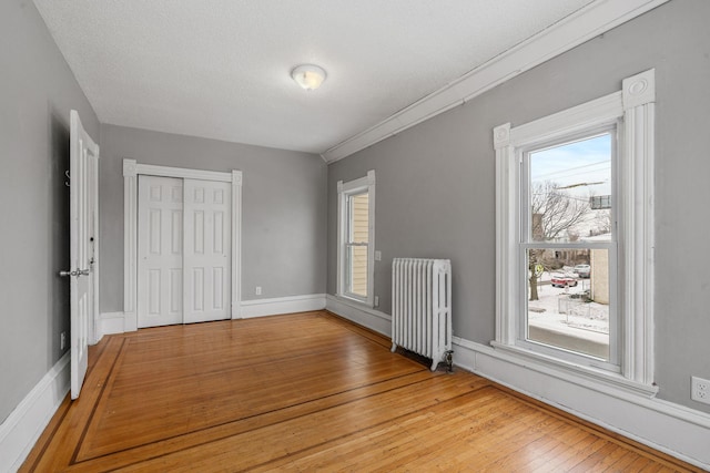 unfurnished bedroom featuring a textured ceiling, radiator, a closet, and light wood-type flooring