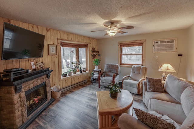 living room with wood walls, hardwood / wood-style flooring, ceiling fan, baseboard heating, and a wall unit AC