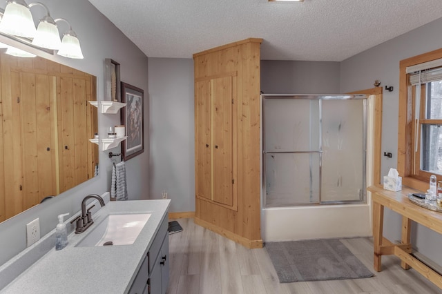 bathroom featuring a textured ceiling, vanity, wood-type flooring, and bath / shower combo with glass door