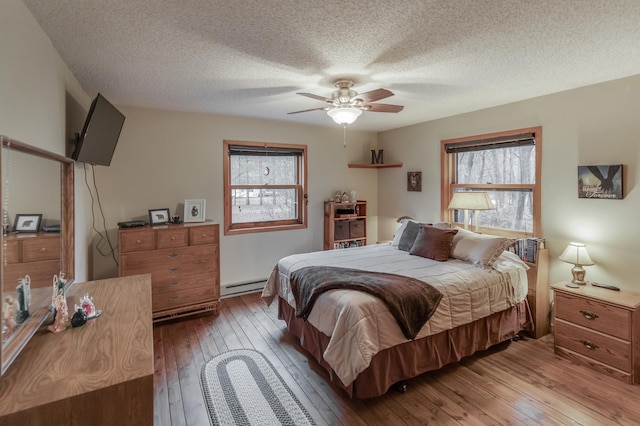 bedroom with baseboard heating, ceiling fan, a textured ceiling, and hardwood / wood-style flooring