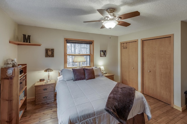 bedroom with a textured ceiling, light hardwood / wood-style floors, ceiling fan, and multiple closets