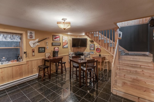 dining area with a textured ceiling, baseboard heating, and wood walls