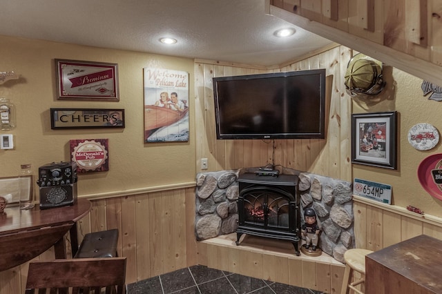 living room featuring a wood stove, wood walls, tile patterned flooring, and a textured ceiling