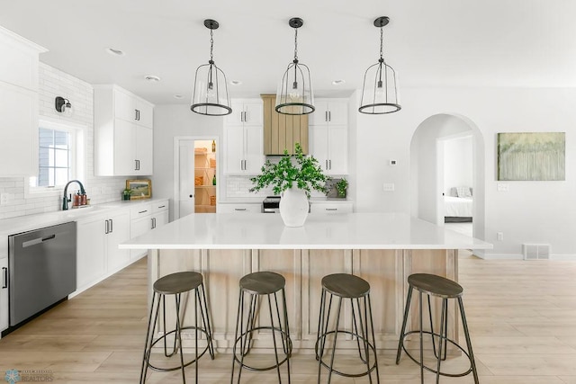 kitchen featuring white cabinetry, a large island, light hardwood / wood-style flooring, stainless steel dishwasher, and decorative light fixtures