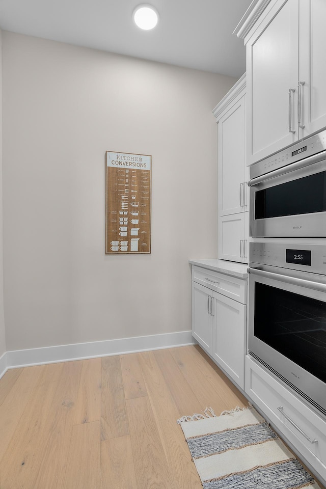 1 Hill Farm Rd Unit 107, North Oaks, MN 55127 - kitchen with double oven, baseboards, light countertops, white cabinetry, and light wood finished floors