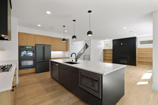 kitchen featuring pendant lighting, light wood-type flooring, built in appliances, sink, and a center island with sink