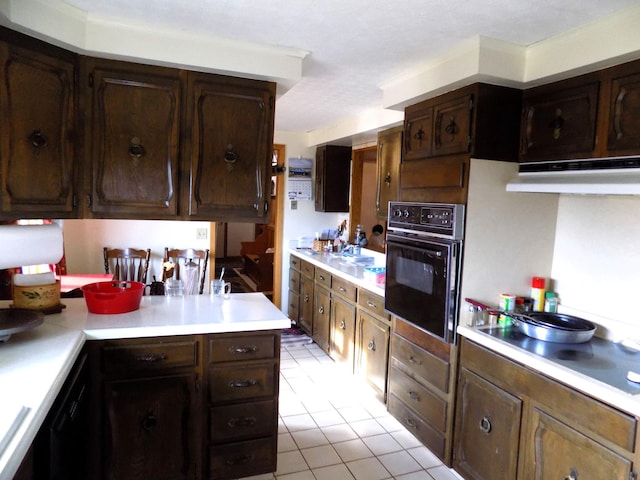 kitchen featuring dark brown cabinets, light tile flooring, and black oven