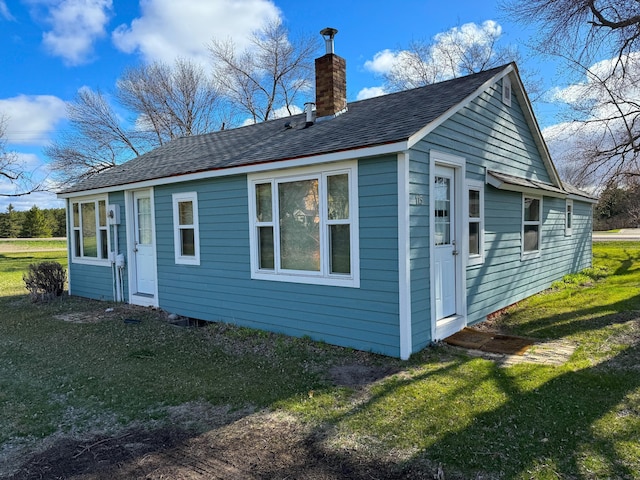 back of property featuring a yard, roof with shingles, and a chimney