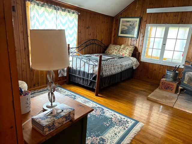 bedroom featuring a wood stove, vaulted ceiling, wooden walls, and wood finished floors