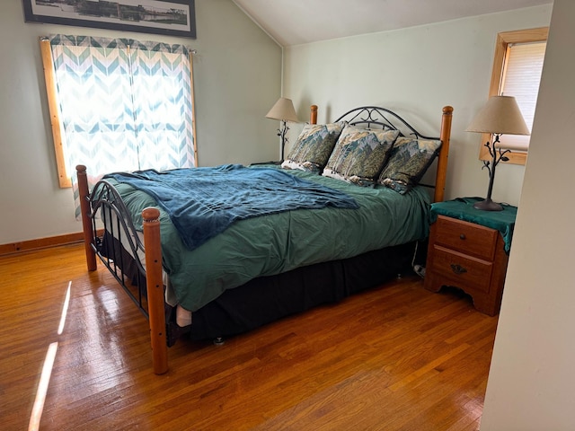 bedroom featuring lofted ceiling, multiple windows, baseboards, and wood finished floors