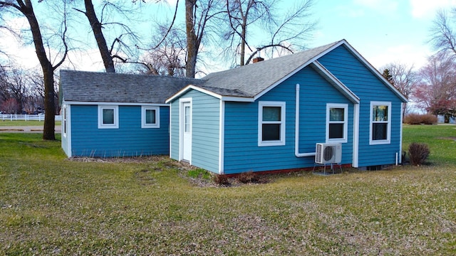 rear view of house with ac unit, a shingled roof, a lawn, and an outbuilding