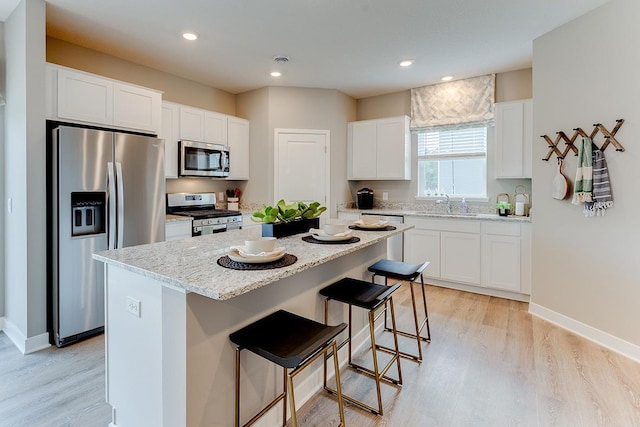 kitchen with a kitchen island, light stone countertops, white cabinets, appliances with stainless steel finishes, and light hardwood / wood-style floors