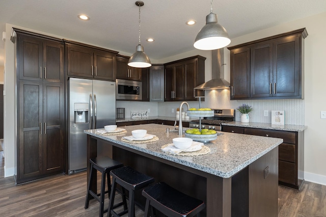 kitchen featuring pendant lighting, dark wood-type flooring, wall chimney range hood, and stainless steel appliances