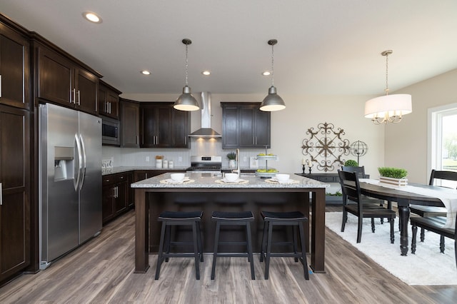 kitchen featuring pendant lighting, appliances with stainless steel finishes, wall chimney range hood, and light stone counters