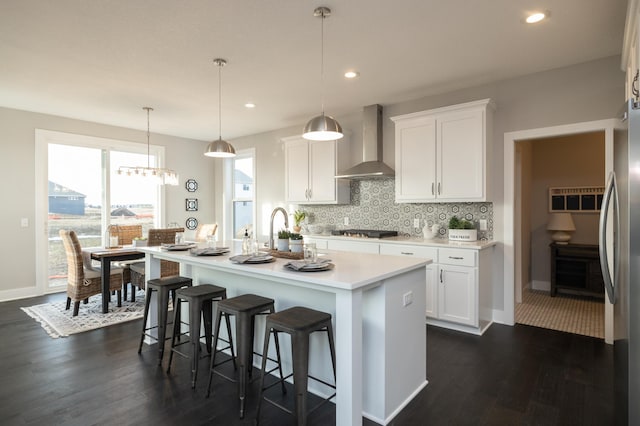 kitchen with a breakfast bar, wall chimney range hood, backsplash, dark hardwood / wood-style flooring, and pendant lighting