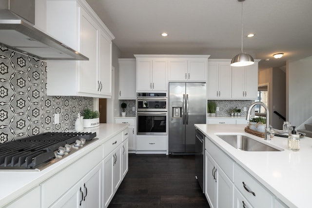 kitchen with decorative light fixtures, white cabinetry, appliances with stainless steel finishes, wall chimney range hood, and sink