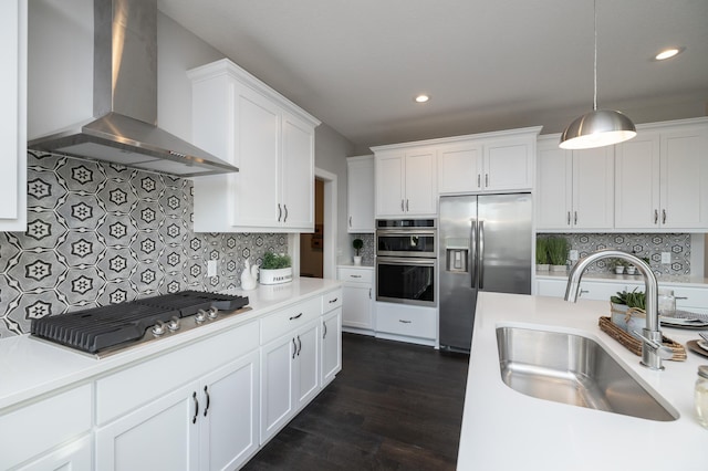 kitchen with wall chimney exhaust hood, sink, white cabinetry, decorative light fixtures, and stainless steel appliances