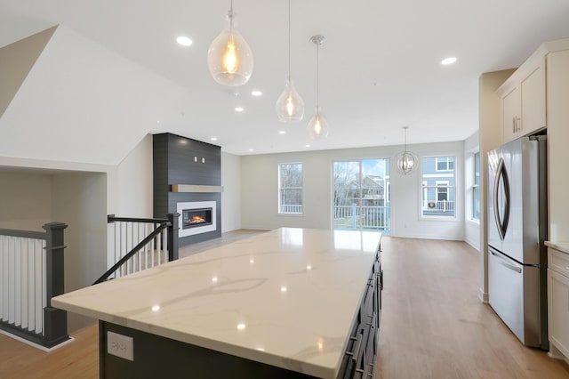 kitchen with a kitchen island, light stone counters, light hardwood / wood-style floors, and stainless steel refrigerator