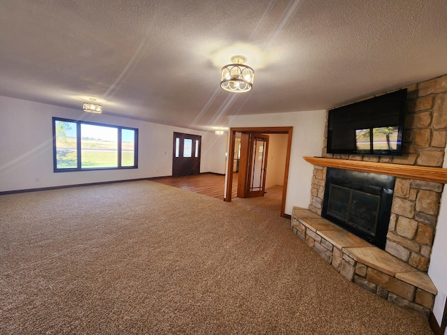 unfurnished living room with baseboards, carpet, a stone fireplace, and a textured ceiling