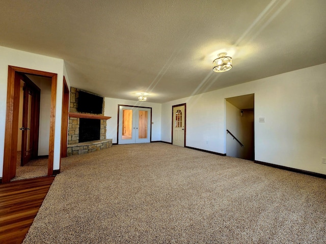 unfurnished living room featuring baseboards, carpet floors, a stone fireplace, french doors, and a textured ceiling