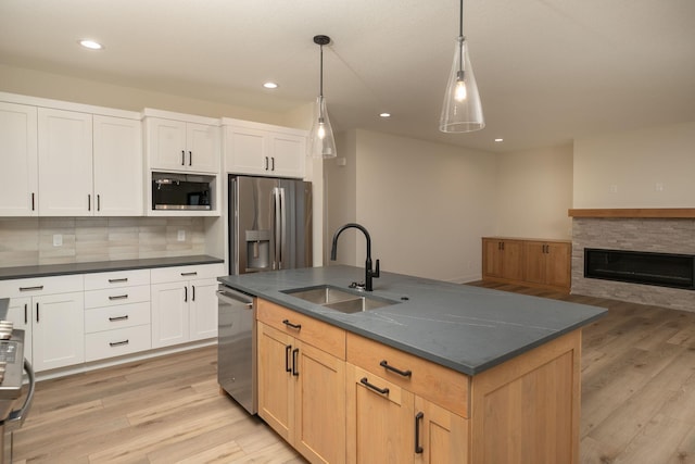 kitchen with an island with sink, sink, white cabinets, pendant lighting, and appliances with stainless steel finishes