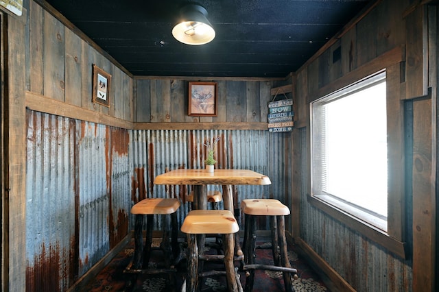 dining space featuring a healthy amount of sunlight, bar, and wooden walls