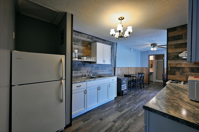 kitchen featuring sink, wood walls, ceiling fan with notable chandelier, and white fridge