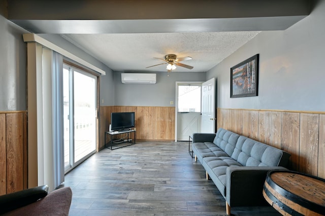 living room with an AC wall unit, a textured ceiling, hardwood / wood-style floors, wood walls, and ceiling fan