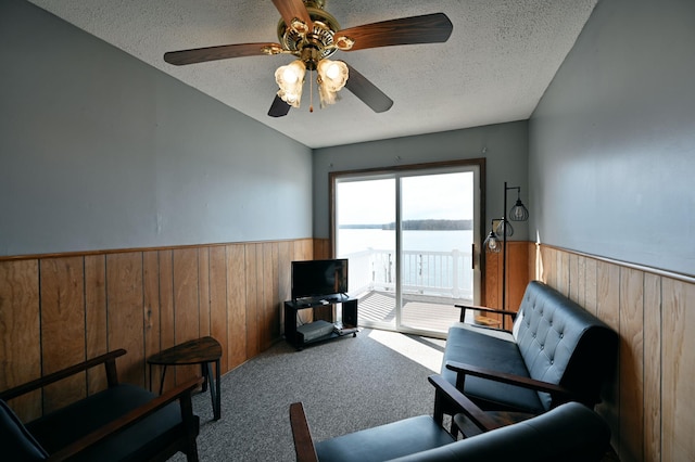 sitting room featuring carpet floors, ceiling fan, wood walls, and a textured ceiling