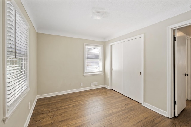 unfurnished bedroom with a textured ceiling, a closet, and dark hardwood / wood-style floors