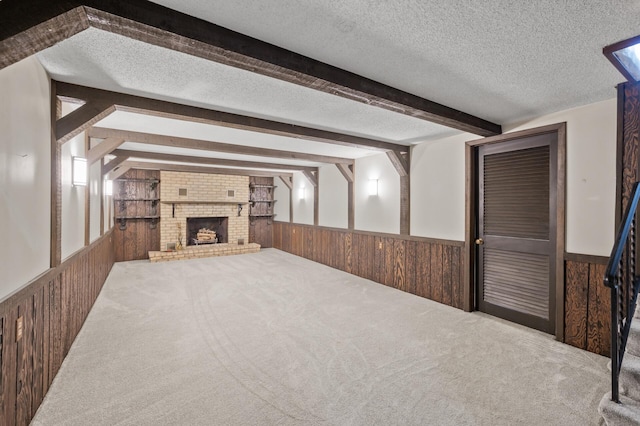 unfurnished living room featuring a textured ceiling, wooden walls, carpet, and beam ceiling