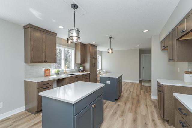 kitchen with sink, a kitchen island, pendant lighting, light hardwood / wood-style floors, and backsplash