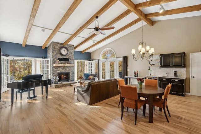 dining room with ceiling fan with notable chandelier, a stone fireplace, high vaulted ceiling, and light hardwood / wood-style floors