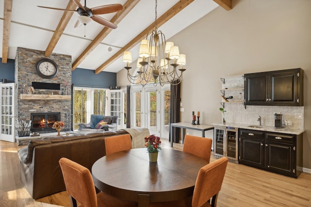 dining area with beverage cooler, high vaulted ceiling, light wood-type flooring, a fireplace, and sink