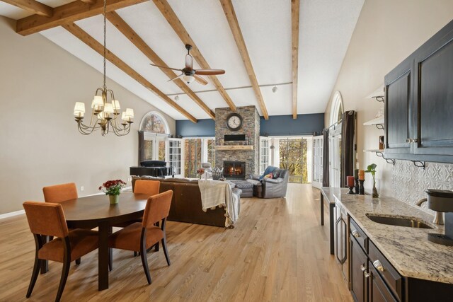 dining area featuring sink, light wood-type flooring, a stone fireplace, beamed ceiling, and high vaulted ceiling